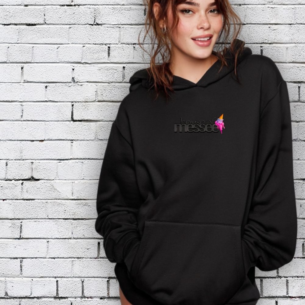 Person wearing a black hoodie with a logo against a white brick wall