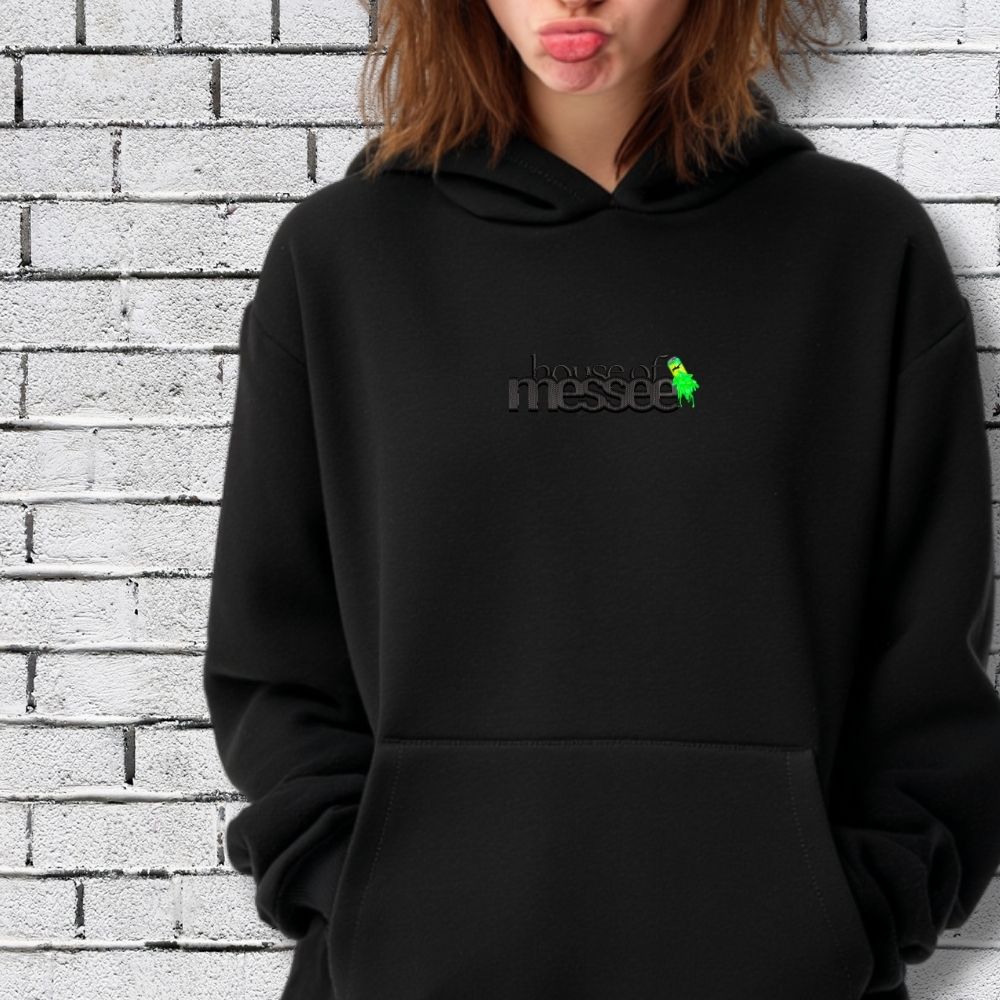 Person wearing a black hoodie with text and logo against a brick wall.